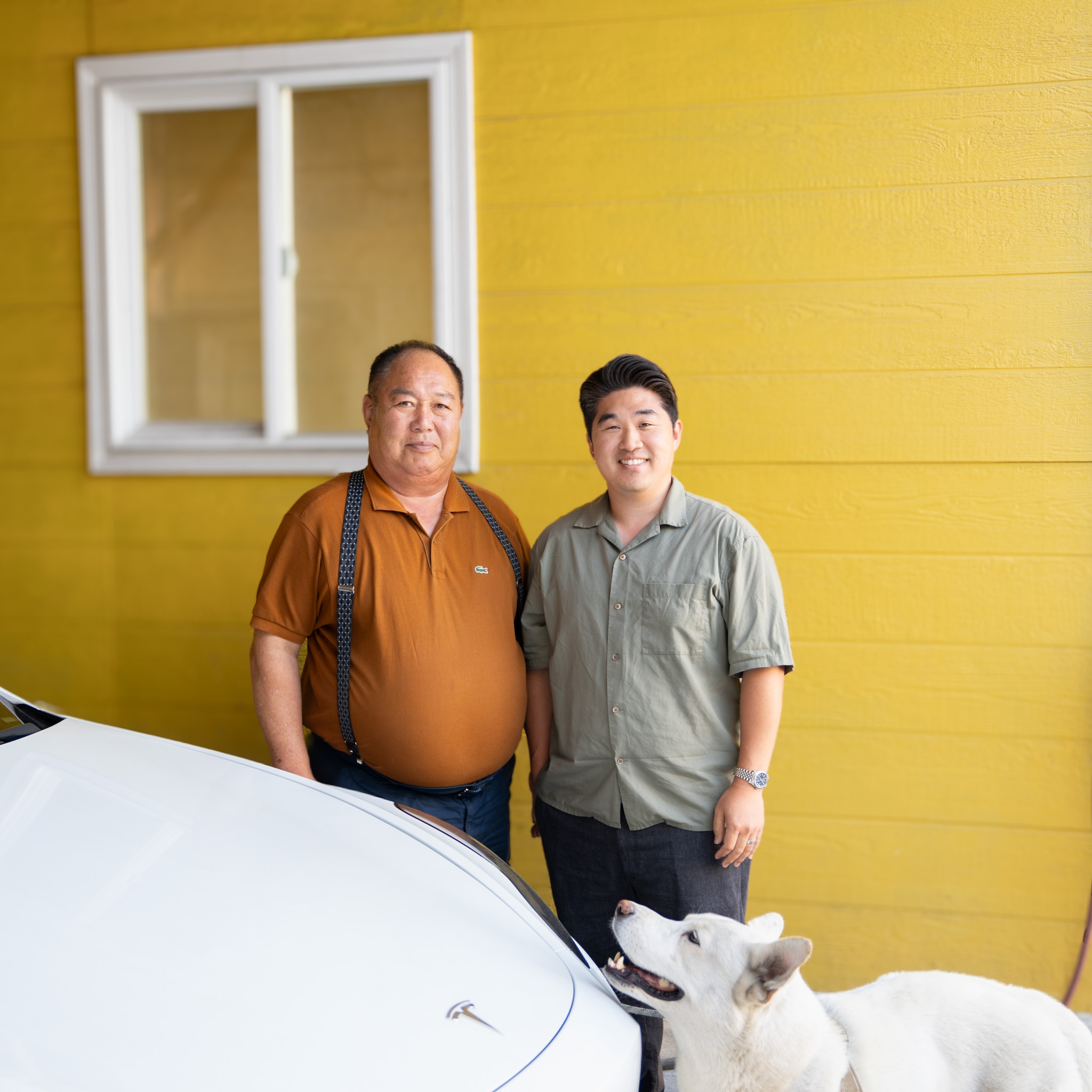 Happy Auto Body owners Roy K. and Bryan B. with their dog beside a freshly repaired white Tesla